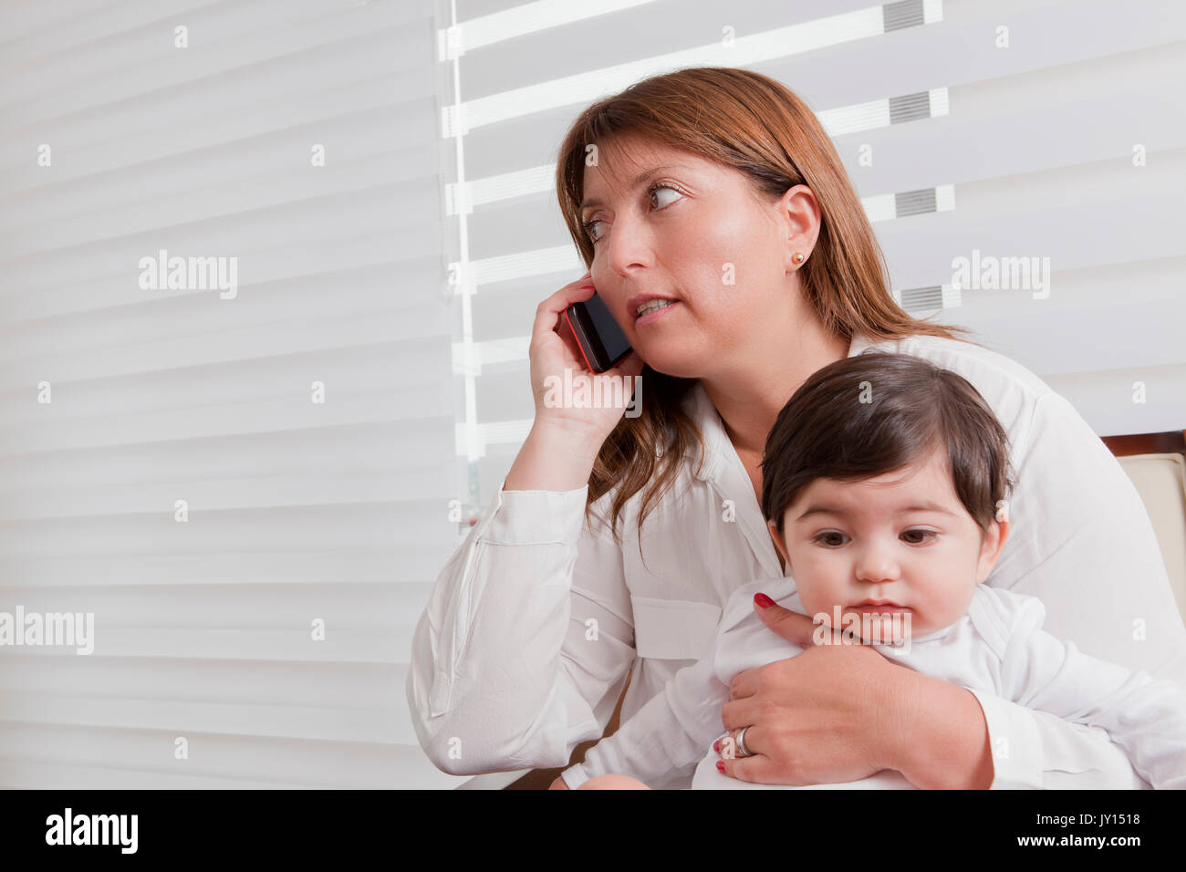 Hispanic mother holding baby boy and talking on cell phone Banque D'Images