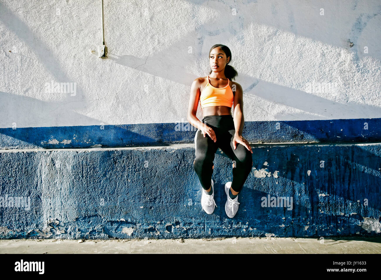 Mixed Race woman sitting on ledge de milieu urbain mur Banque D'Images
