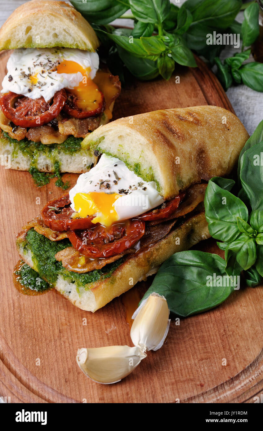 Ciabatta grillé au pesto, tranches de bacon, tomates séchées au soleil et œuf poché Banque D'Images