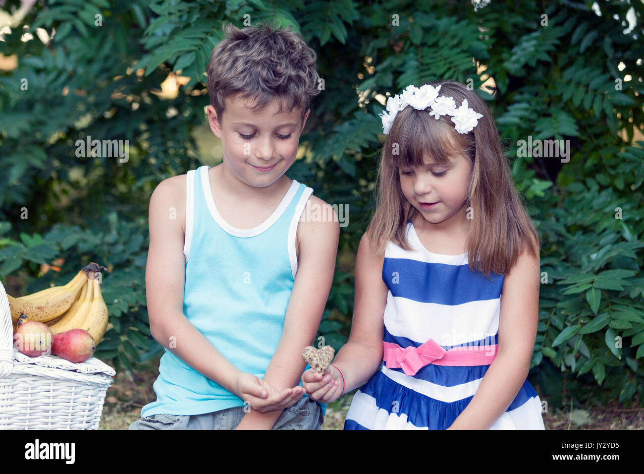 Mignon Petit Garçon Et Fille S'asseoir Dans L'herbe Et Jouer. La Petite Fille Le Garçon Donne Un Mignon Petit Garçon Et Fille S'asseoir Dans L'herbe Et Jouer. La Petite Fille Le Garçon Donne Un