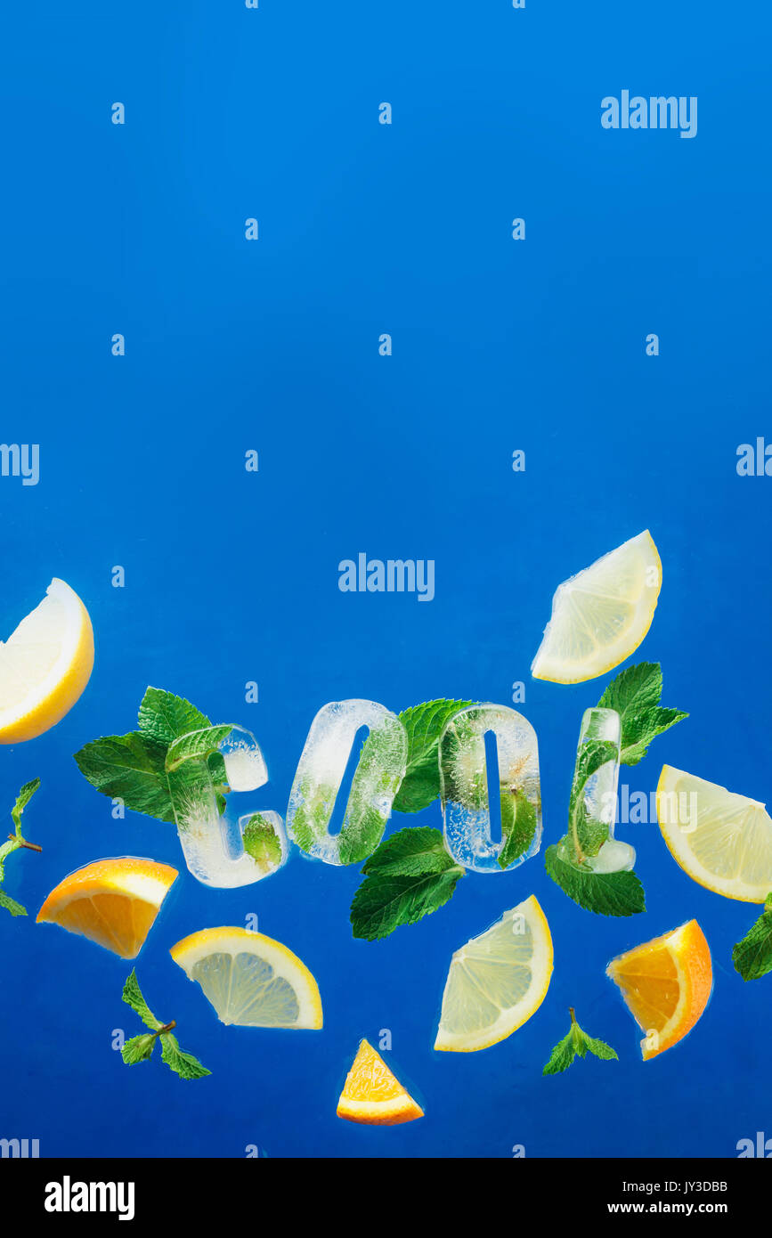 Ice Cube congelé un lettrage en feuilles de menthe, de tranches de citron et d'oranges sur un fond bleu . texte dit cool. Banque D'Images