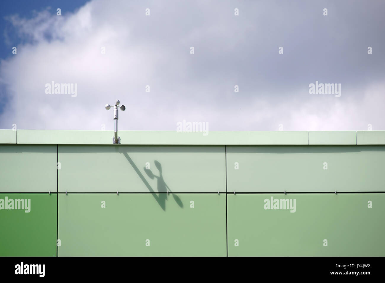 L'hélice d'un capteur de vent sur le bord du toit d'un immeuble moderne jette des ombres. Banque D'Images