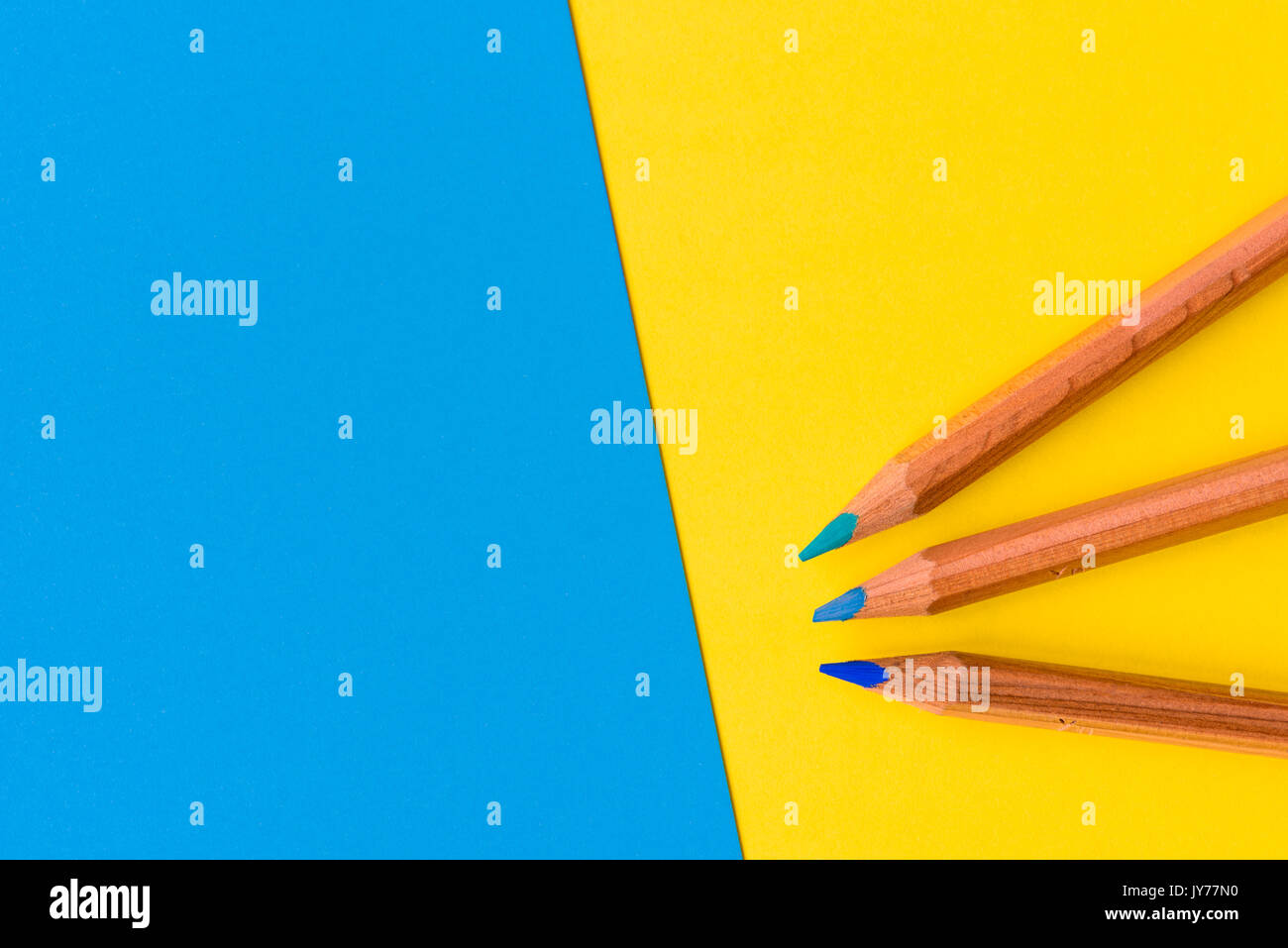 Trois crayons en bois avec une pointe de bleu et jaune contre un fond bleu avec copie espace pour le texte. Banque D'Images