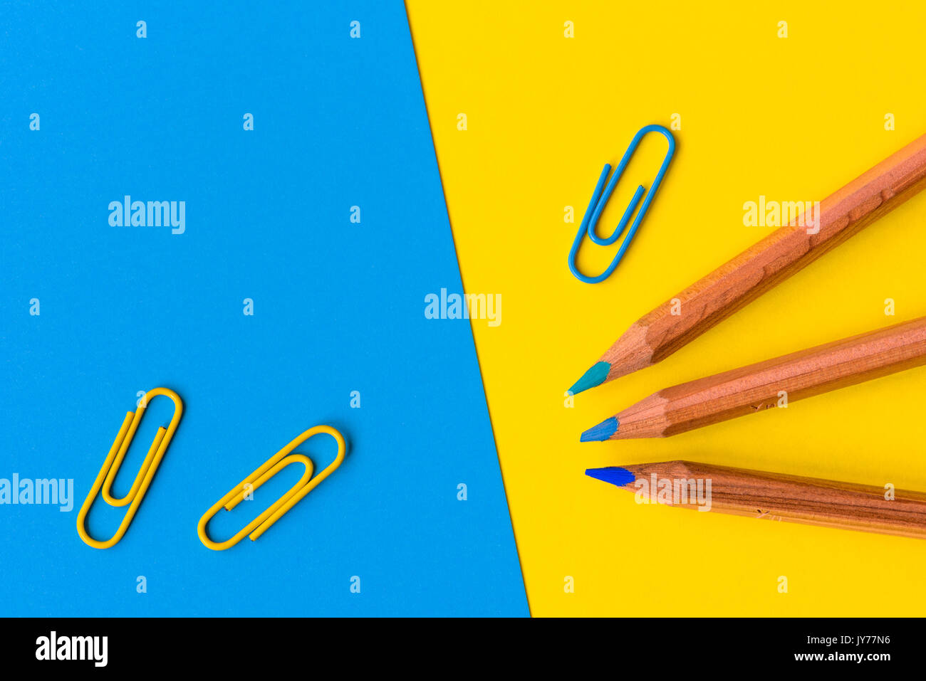 Trois crayons en bois avec une pointe de bleu et bleu et jaune des trombones contre un fond bleu et jaune avec copie espace pour le texte. Banque D'Images