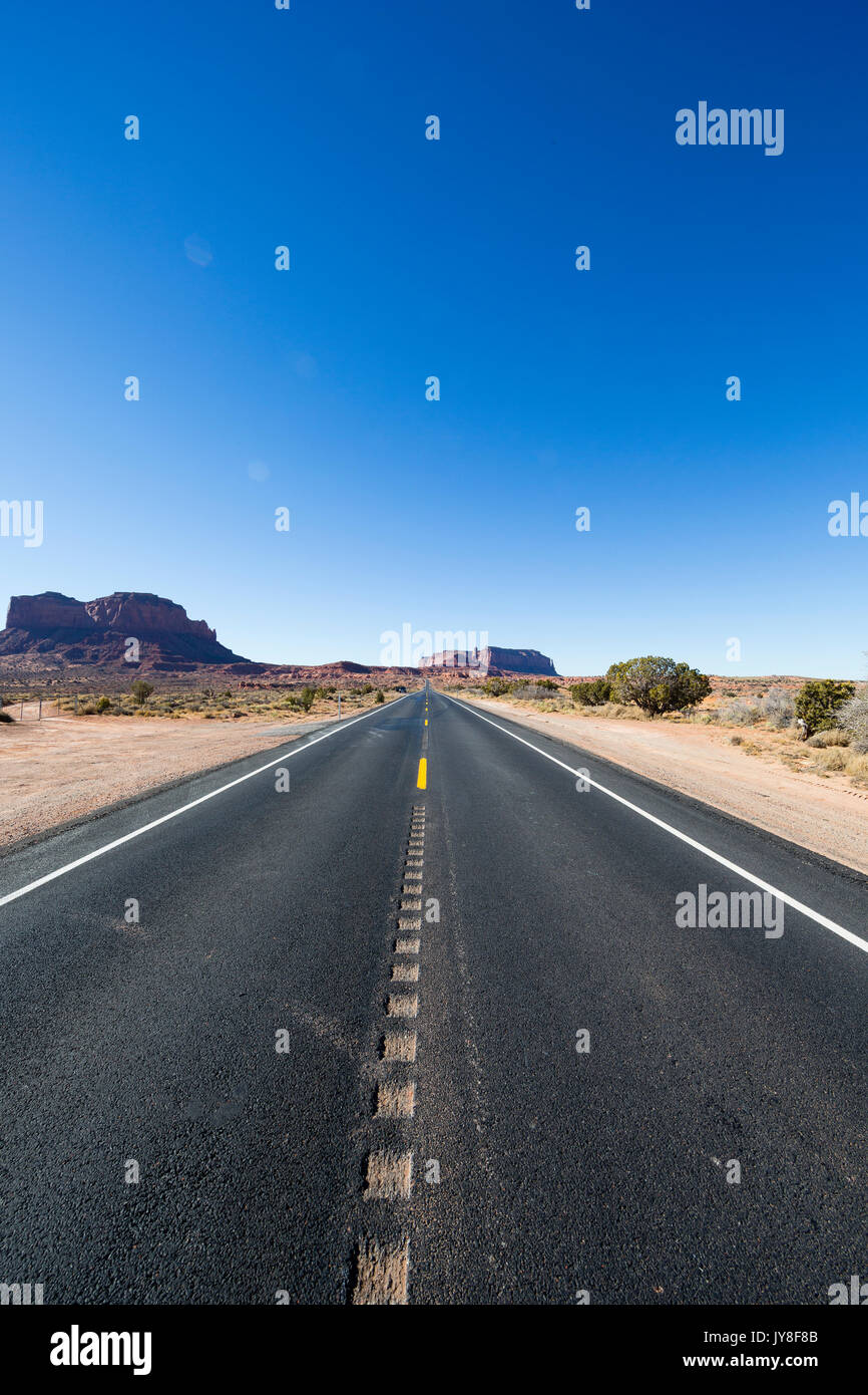 L'Utah, USA. La route à deux voies qui s'étend à l'horizon avec Monument Valley dans l'arrière-plan lointain. Banque D'Images
