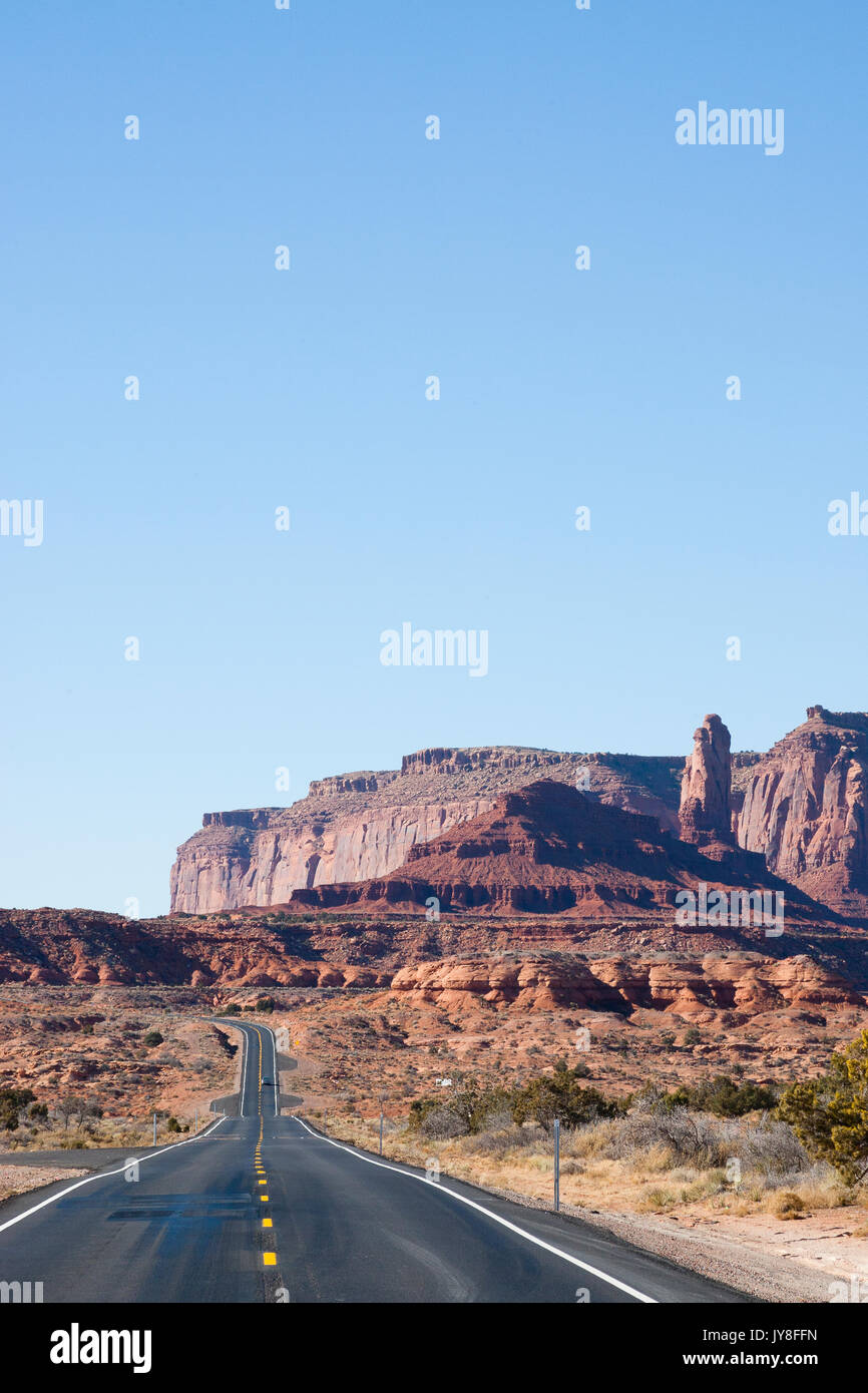 L'Utah, USA. La route à deux voies qui s'étend à l'horizon avec Monument Valley dans l'arrière-plan lointain. Banque D'Images
