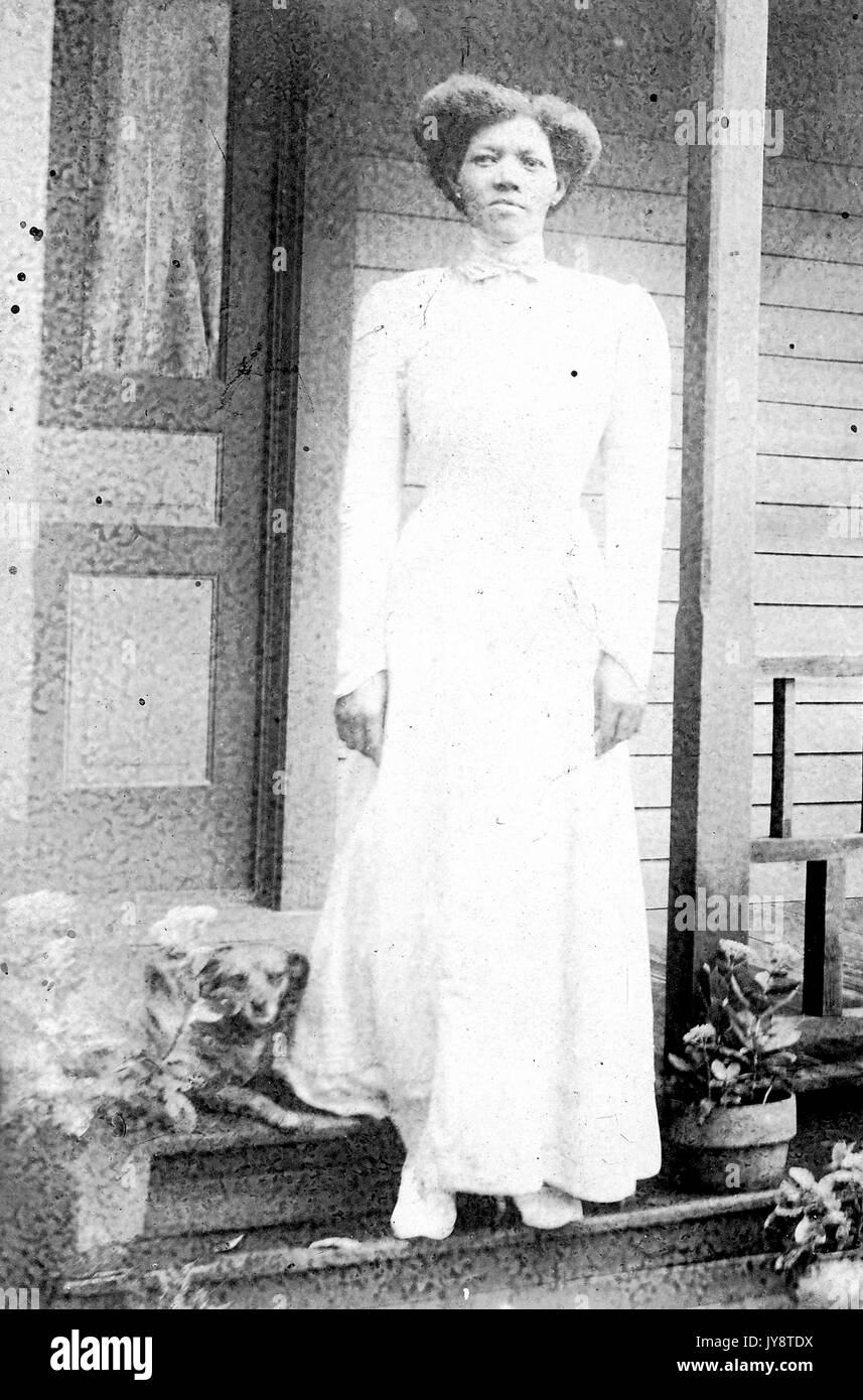 African American Woman in white dress, pleine longueur portrait, debout sur l'escalier d'une maison, avec un petit chien à ses pieds, 1944. Banque D'Images