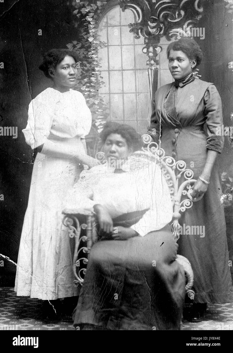 Portrait de trois femmes afro-américaines, deux debout derrière l'autre assis dans une chaise, arborent des posés en face d'une fresque-comme toile de fond, la femme la plus à gauche dans une robe blanche, et les deux autres en robes sombres, avec toutes les expressions du visage en blanc, 1920. Banque D'Images