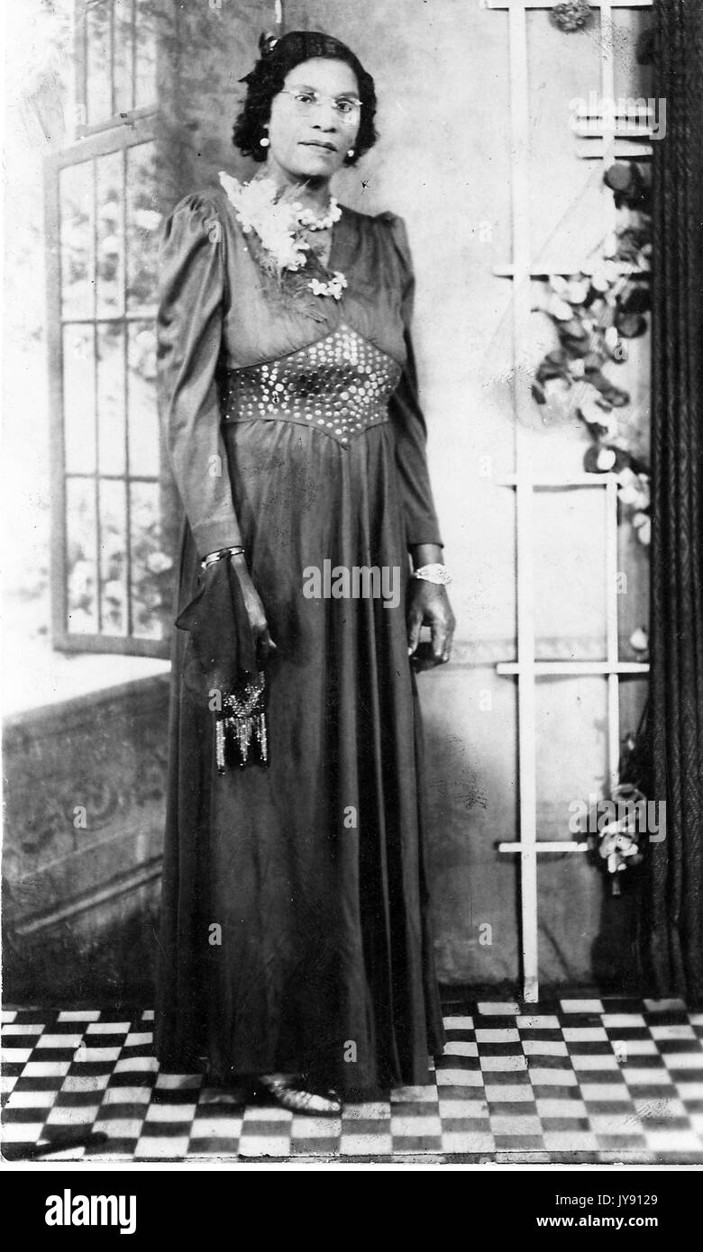 Portrait complet de la femme afro-américaine mature en robe sombre, debout à côté de la fenêtre ouverte, avec une expression faciale sérieuse, portant des lunettes, 1915. Banque D'Images
