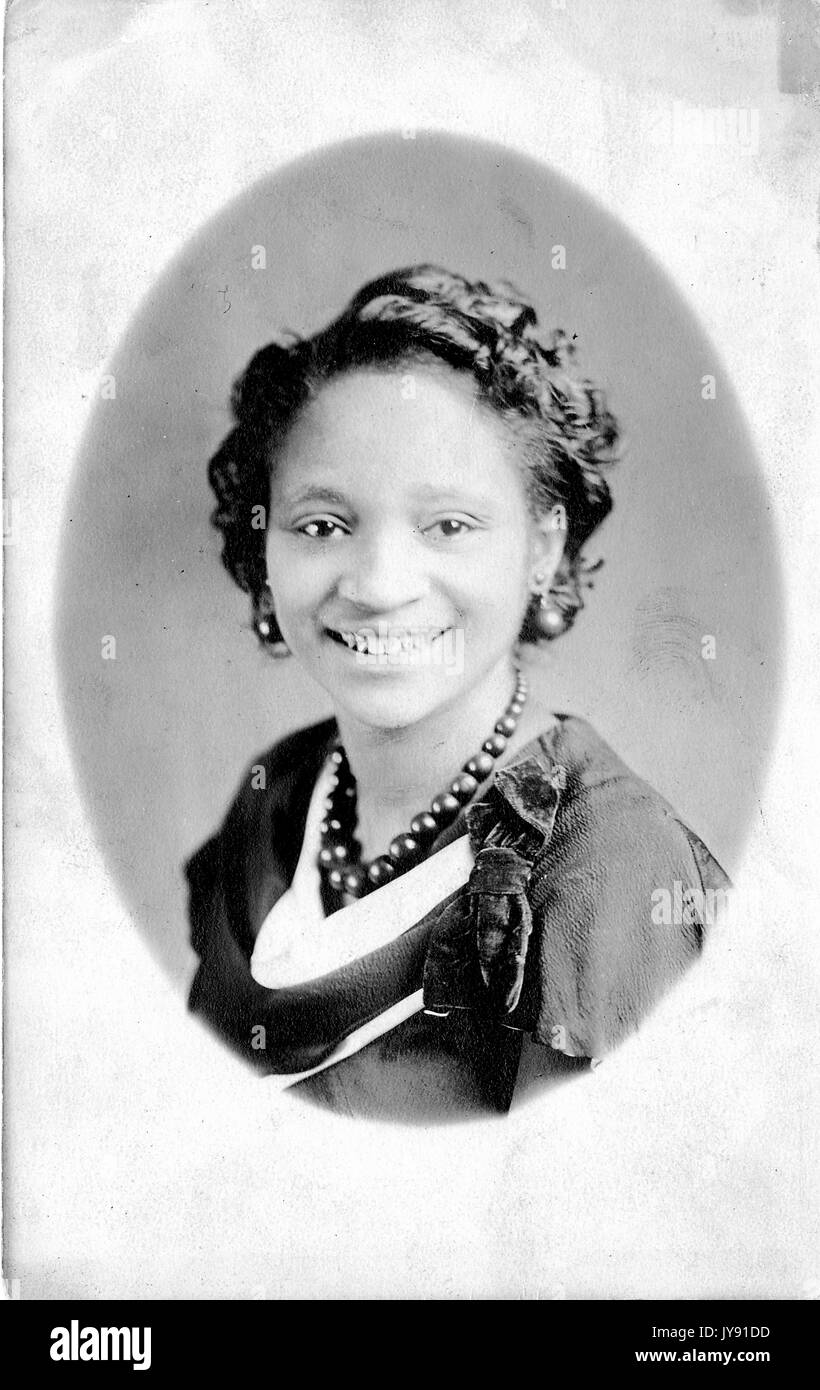 Portrait of young African American Woman, portant un collier, boucles d'oreilles et une robe sombre avec un archet, smiling, 1920. Banque D'Images