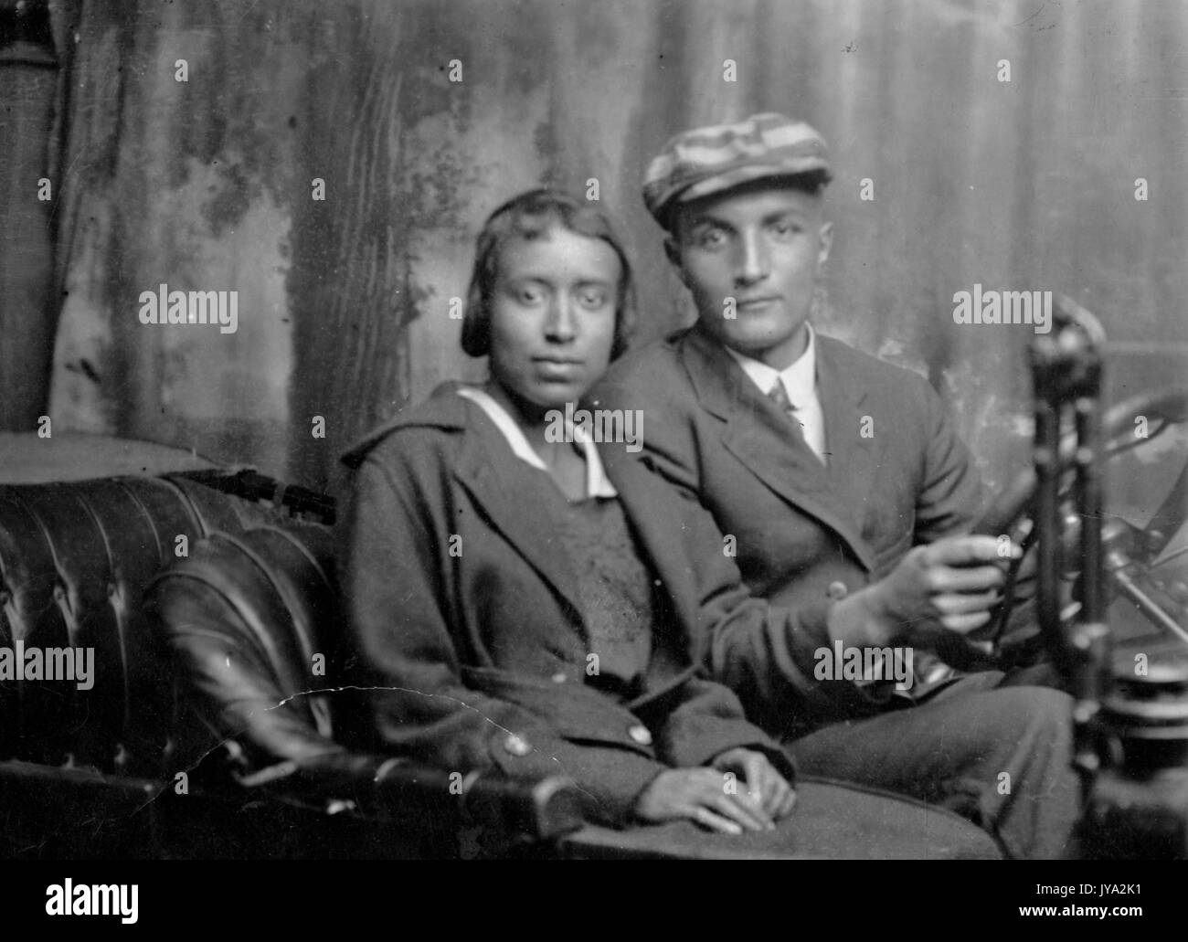 African-american couple posant pour une photo derrière le volant d'une automobile, dans un studio de photographie, en face d'une toile peinte, 1925. Banque D'Images