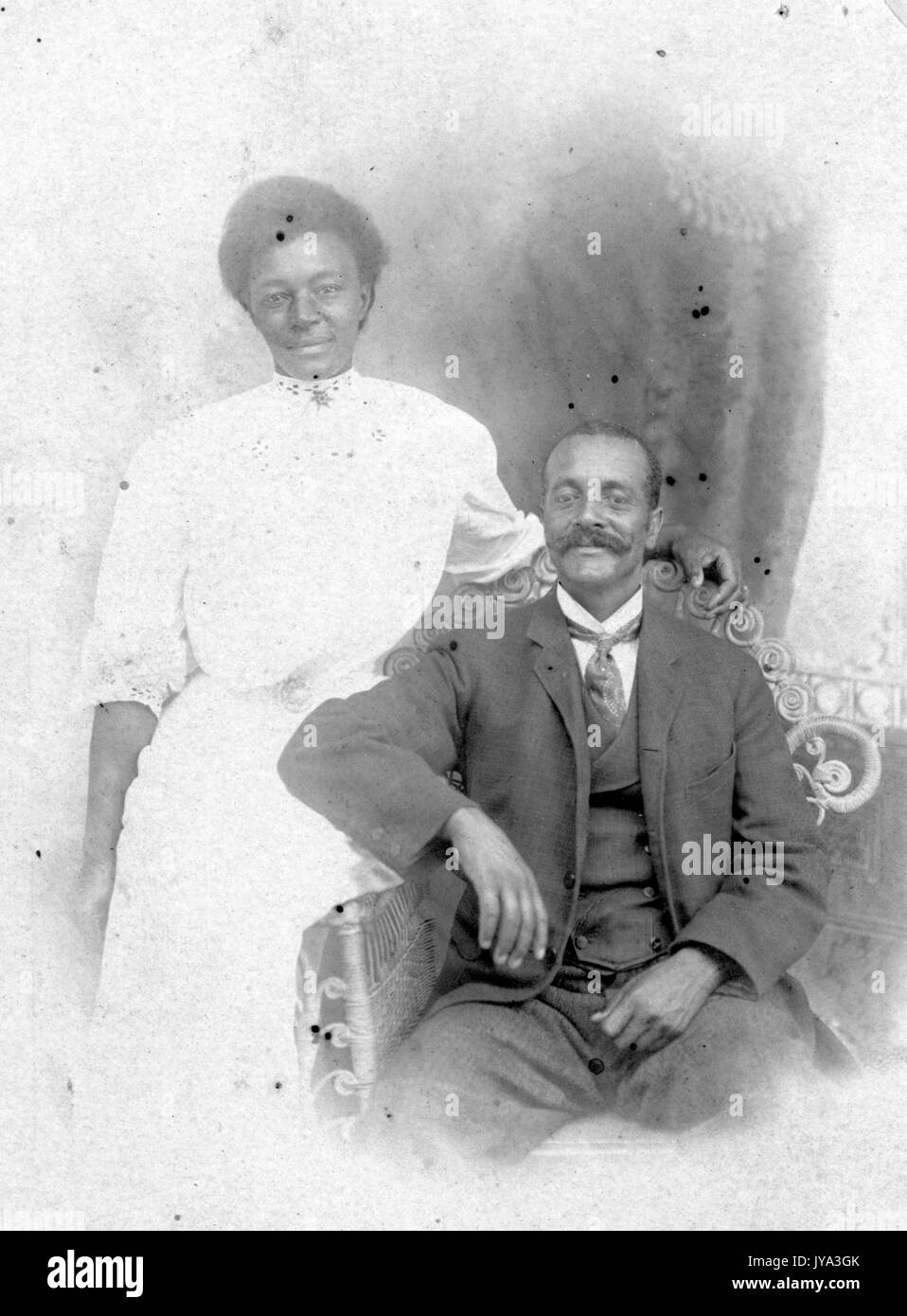 Couple afro-américain posant pour une photographie de portrait, homme assis sur un banc et portant un costume et une cravate, femme portant une robe blanche debout derrière lui, Atlantic City, New Jersey, 1932. Banque D'Images