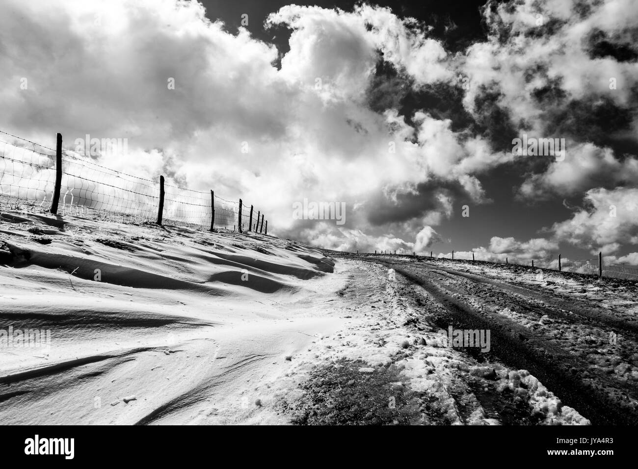 Une route de montagne avec de la neige sur le côté, sous un ciel profond avec des nuages blancs Banque D'Images