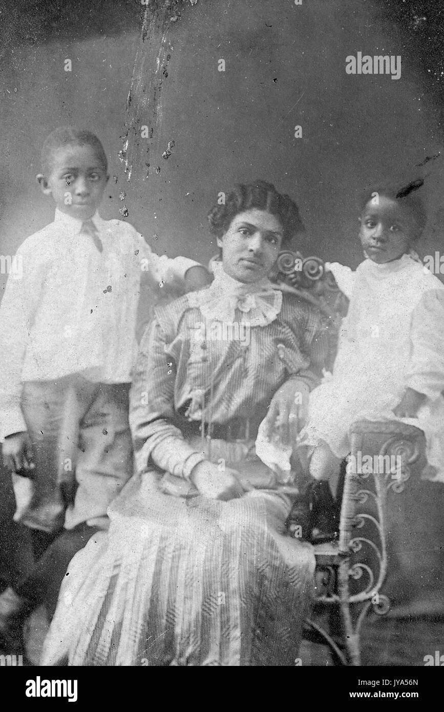 Mère afro-américains dans des tenues de poser pour un portrait de studio, assis sur une chaise, ses deux enfants debout à ses côtés, un garçon et une fille, le 20 août 1910. Banque D'Images