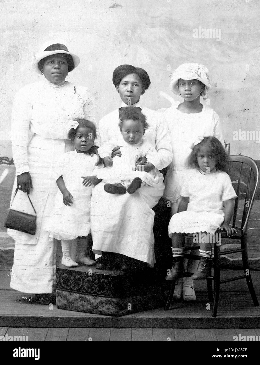 La famille afro-américaine, une mère debout avec son cinq filles et posant pour un portrait de studio, tous vêtus de blanc, la mère tenant un sac à main et portant un chapeau, ses filles d'âges différents assis sur des chaises, 1925. Banque D'Images