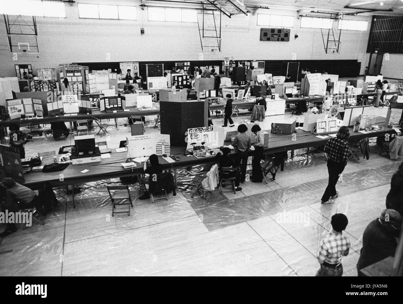 Un gymnase d'école accueillant une foire scientifique, avec plusieurs personnes marchant à travers les rangées de tables alignées et lisant les nombreux triplis et affiches avec des matériaux démonstratifs pour chaque projet de foire scientifique à l'Université Johns Hopkins, Baltimore, Maryland. 1975. Banque D'Images