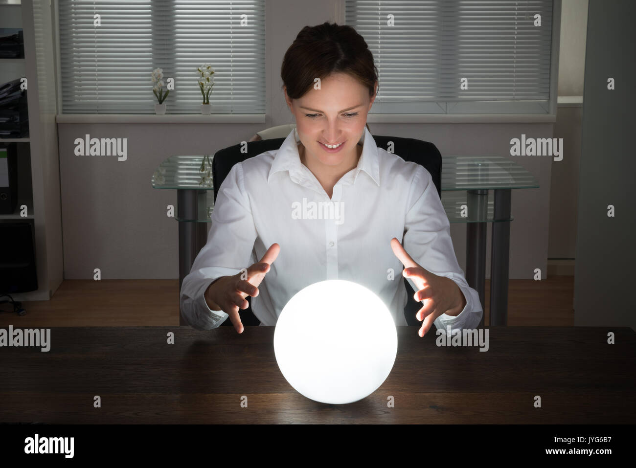 Young Businesswoman Looking dans l'avenir dans une boule de cristal In Office Banque D'Images