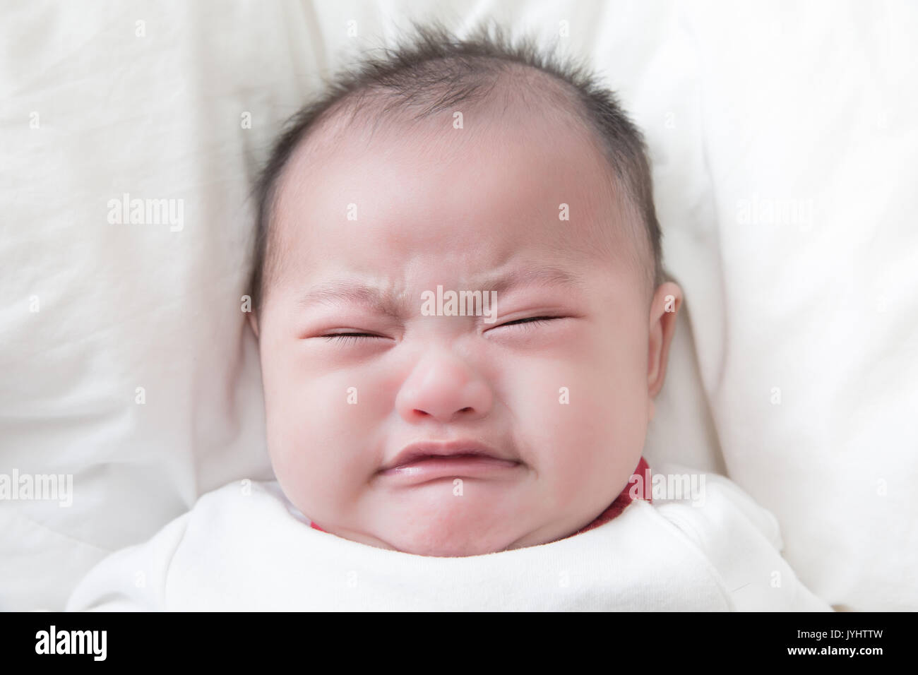 Asian baby boy crying on lit blanc Banque D'Images
