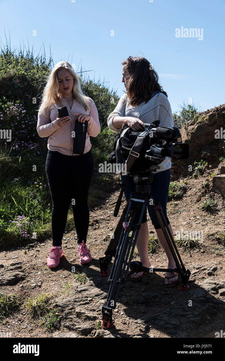 Une jeune journaliste de télévision et de l'appareil photo sur une femme news gathering affectation dans l'île de Sark, bailliage de Guernesey dans les îles de la Manche, la Grande-Bretagne. Banque D'Images
