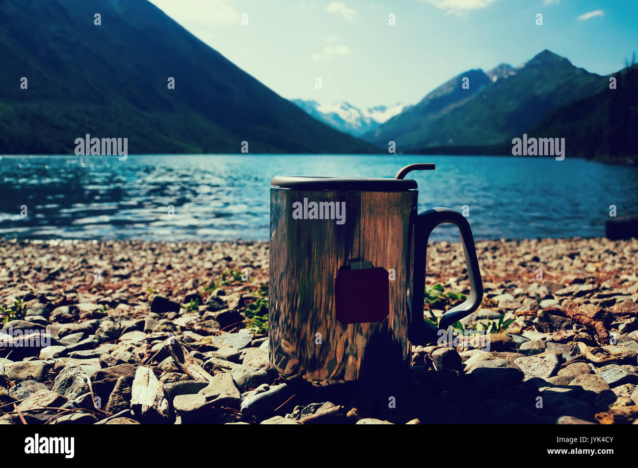 Metal thermo mug d'eau sur pierres, sur fond flou belles montagnes. La notion de fraîcheur et de la pureté de la nature sauvage. Banque D'Images