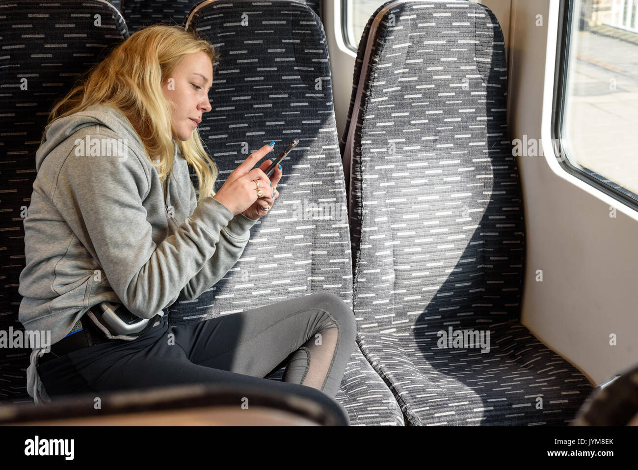 Jeune femme blonde dans un train à l'aide de son smartphone portant des vêtements de sport Banque D'Images