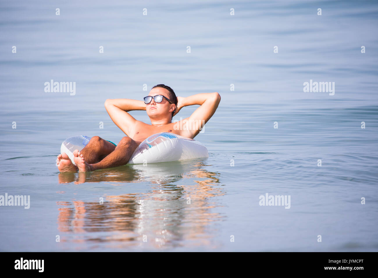 Jeune homme à lunettes avec un verre de bière flottant sur l'anneau de caoutchouc dans l'eau de mer Banque D'Images