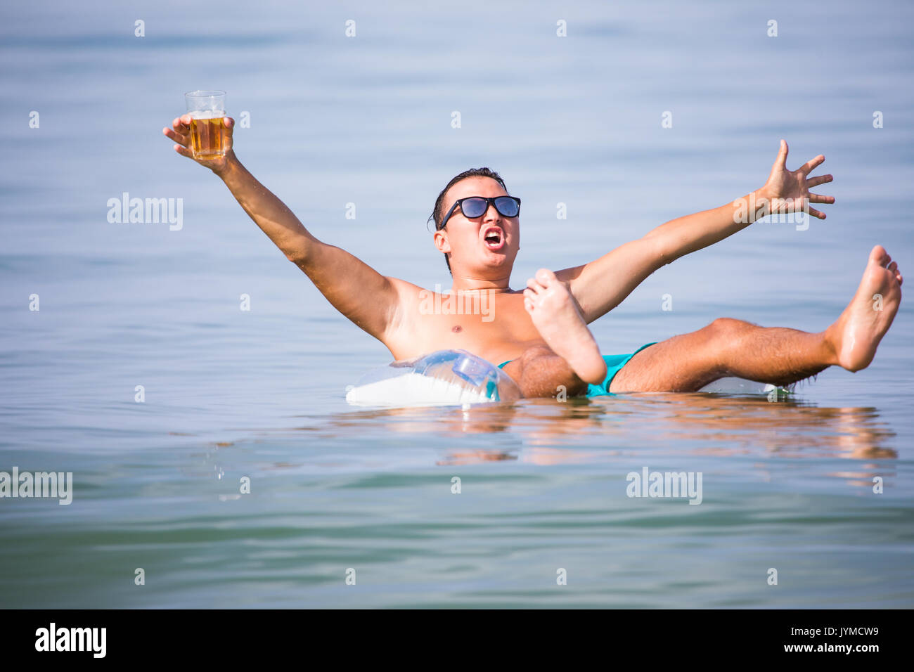 Bel homme natation sur bague en caoutchouc en mer avec verre de bière et de bonne humeur l'été vocation Banque D'Images