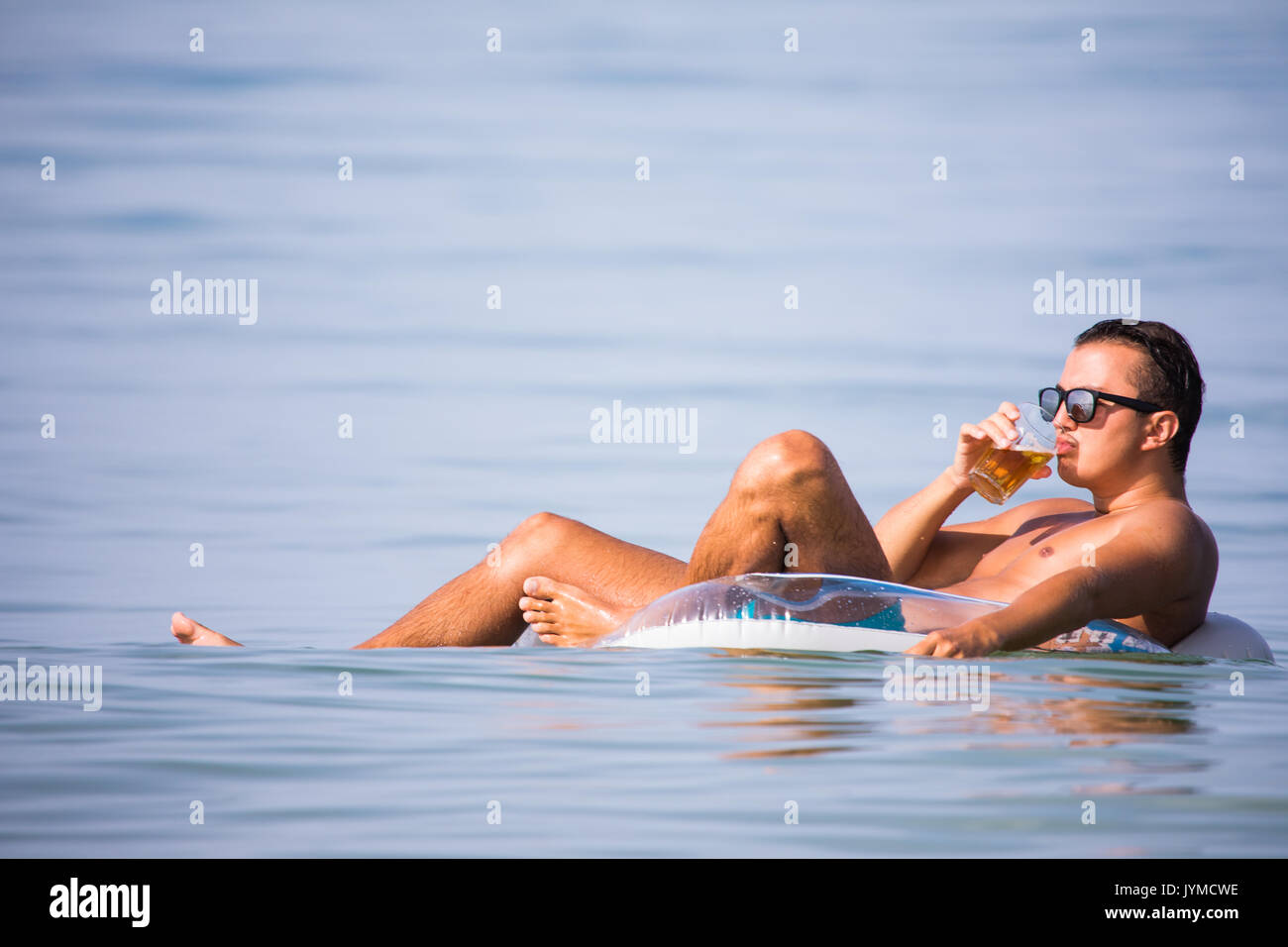 Bel homme natation sur bague en caoutchouc en mer avec verre de bière et de bonne humeur l'été vocation Banque D'Images