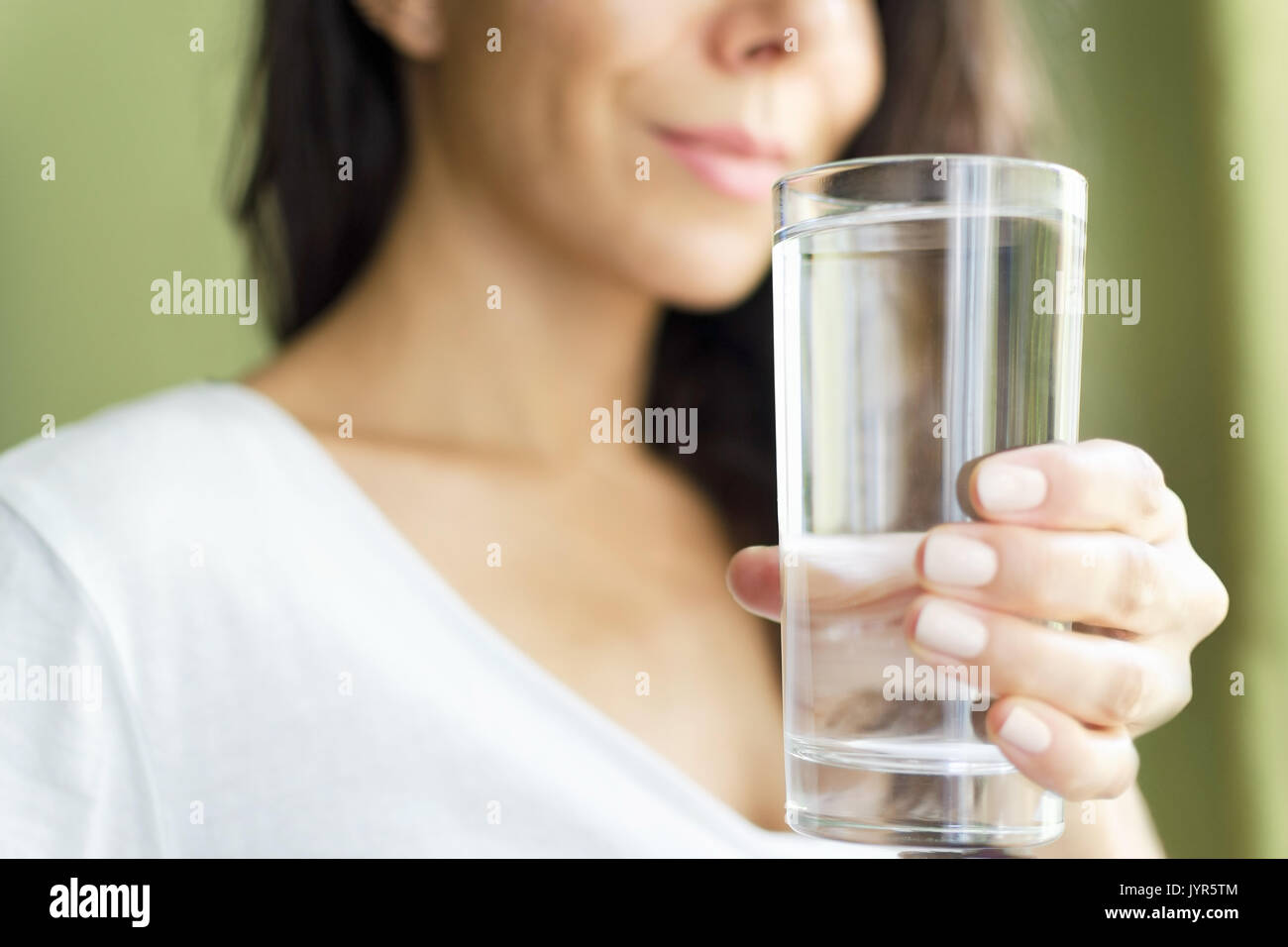 Fille floue dans un T-shirt blanc tenant un verre avec de l'eau et sourit. Fond vert Banque D'Images