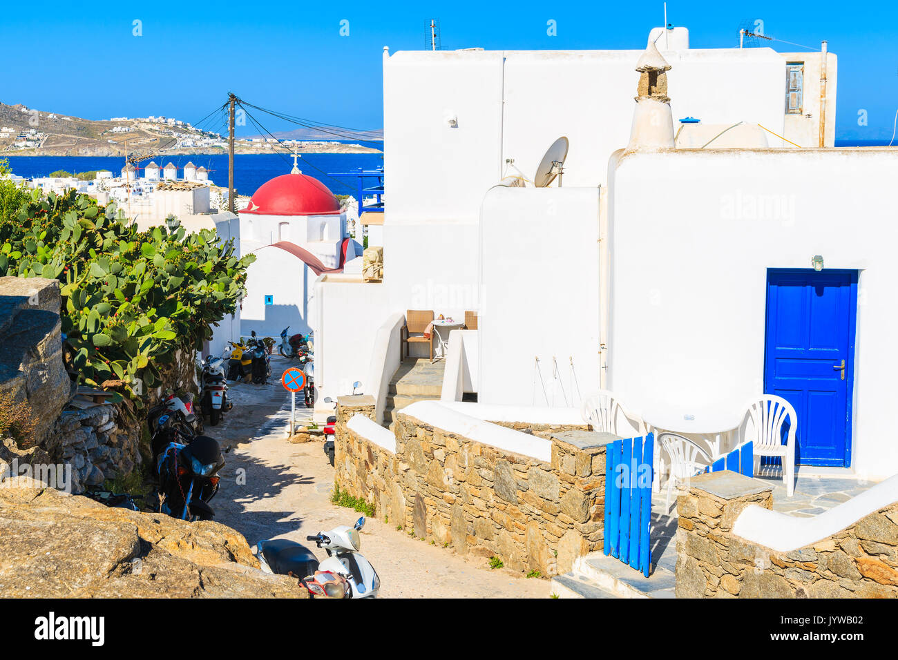 Blanc typique maison grecque avec porte bleue et l'église dans la distance dans la belle ville de Mykonos, Cyclades, Grèce Banque D'Images