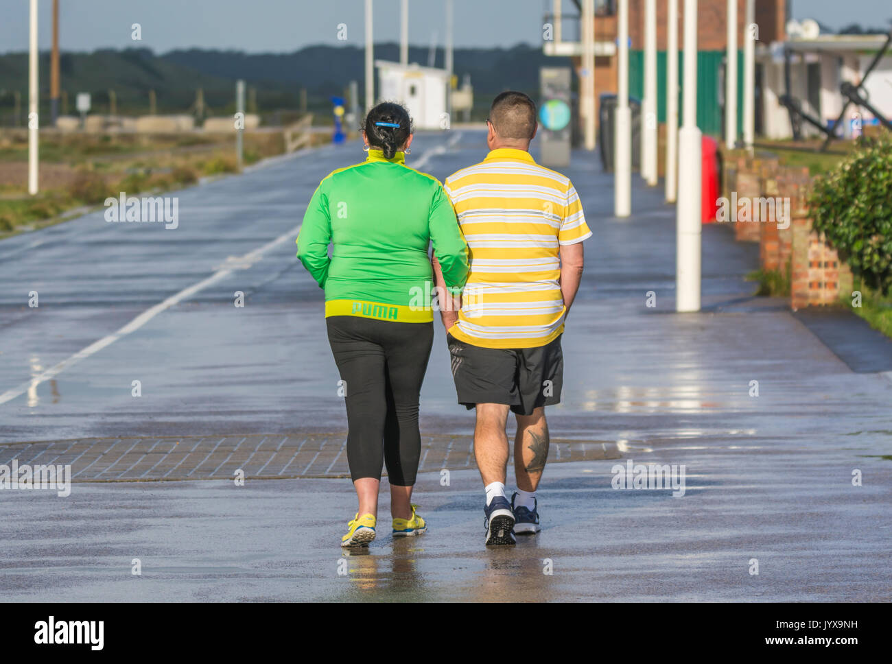 Couple en train de marcher sous la pluie le long d'une promenade de bord de mer. déserte autrement Banque D'Images