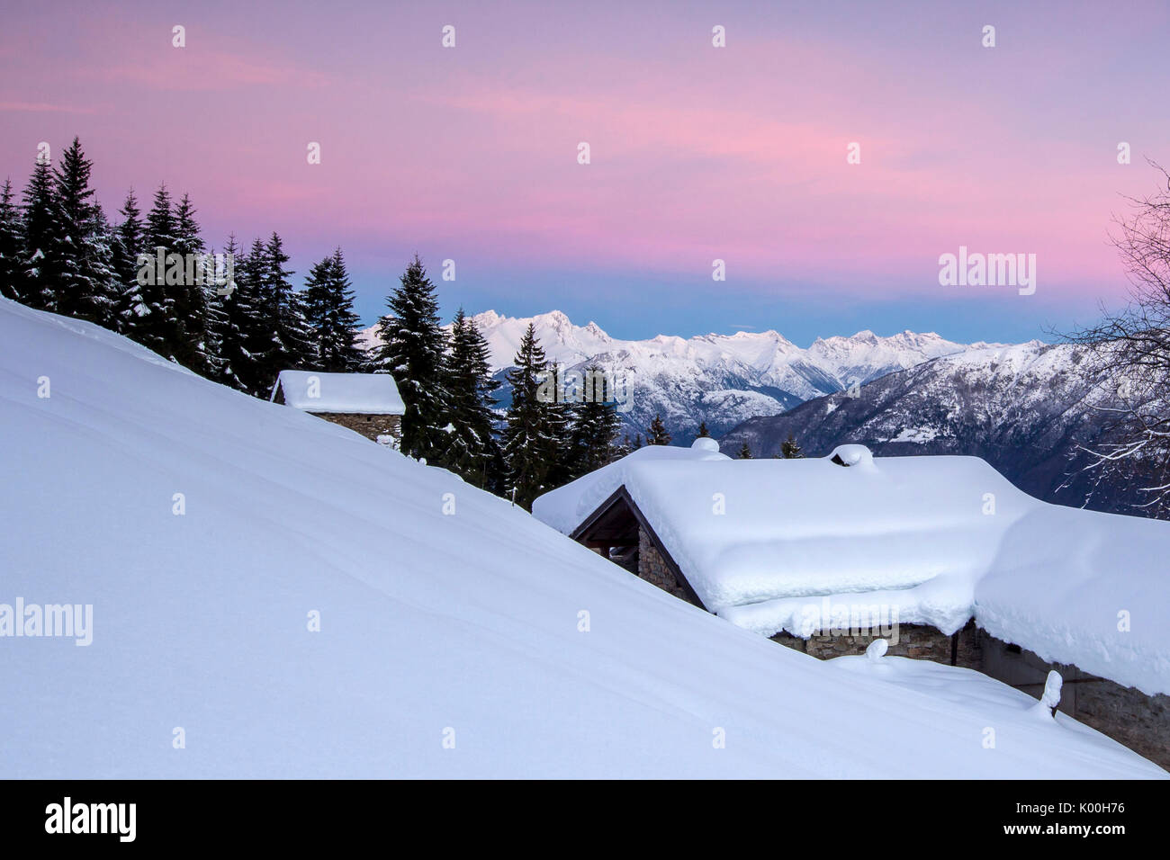 Ciel rose à l'aube au-dessus de huttes couvertes de neige et d'arbres Tagliate Di Sopra Gerola Valley Alpes Orobie Valtellina Lombardie Italie Europe Banque D'Images