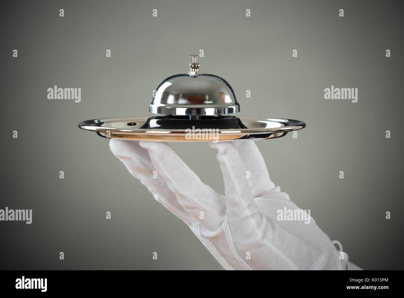 La main coupée de waiter holding service Bell dans le bac à l'arrière-plan gris Banque D'Images