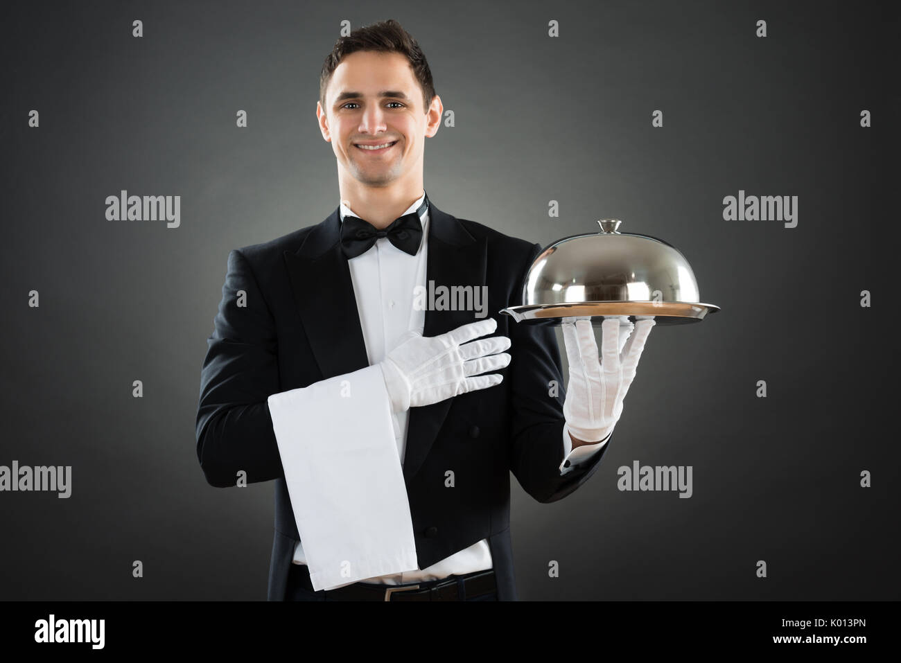 Portrait of happy waiter avec bac et permanent contre l'arrière-plan gris serviette Banque D'Images