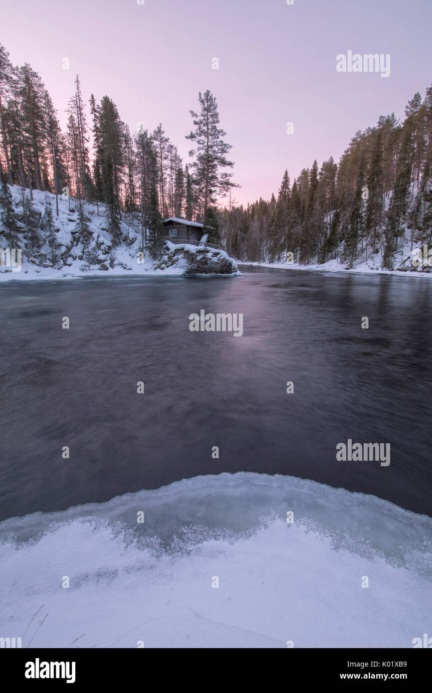 Une cabane en bois entouré par la rivière gelée et Snowy Woods au crépuscule Juuma Myllykoski région Laponie Finlande Europe Banque D'Images