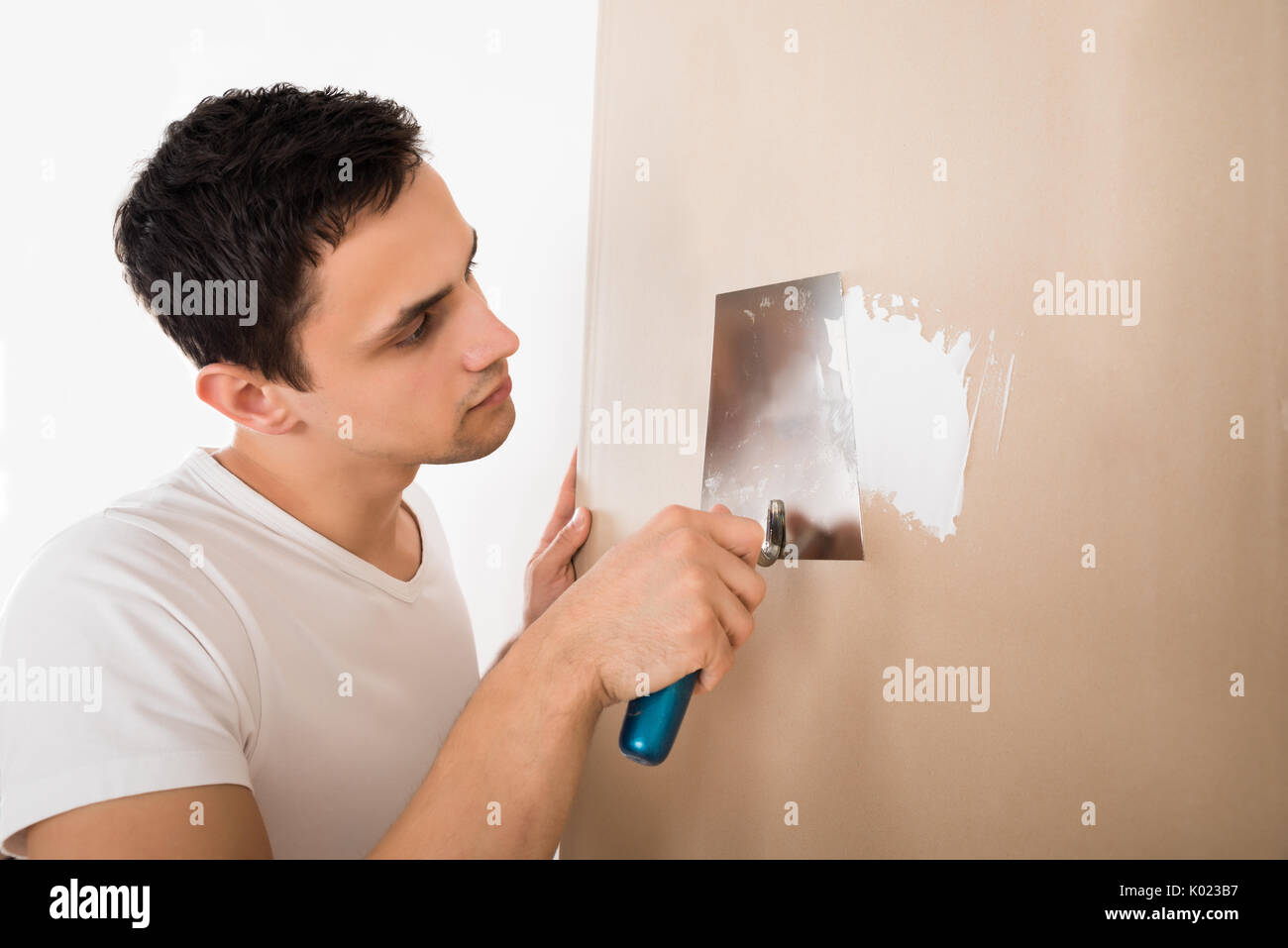 Jeune homme à l'aide d'une spatule sur mur blanc à la maison Banque D'Images