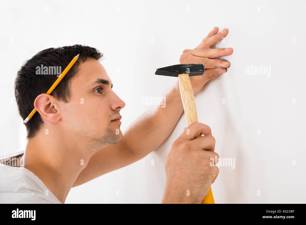 Vue latérale du jeune homme hammering nail sur mur blanc à la maison Banque D'Images