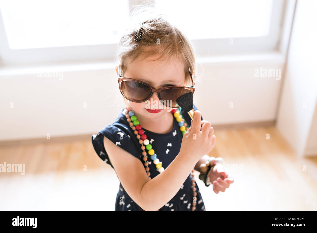 Jolie petite fille en robe et big Sunglasses at home. Banque D'Images