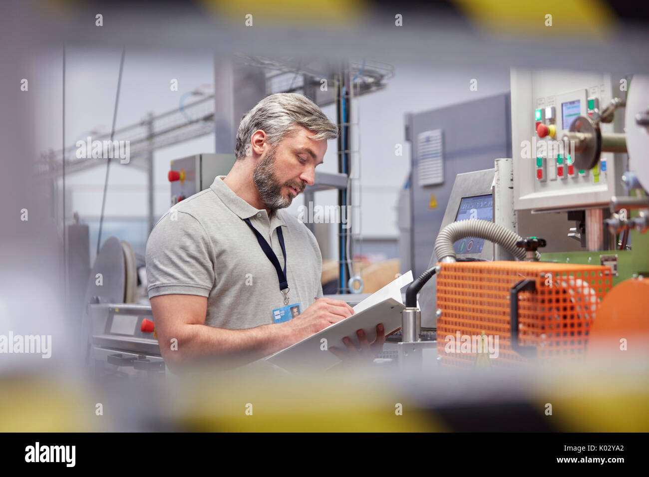 Surveillant masculin avec presse-papiers au panneau de commande de machines dans l'usine de fibre optique Banque D'Images