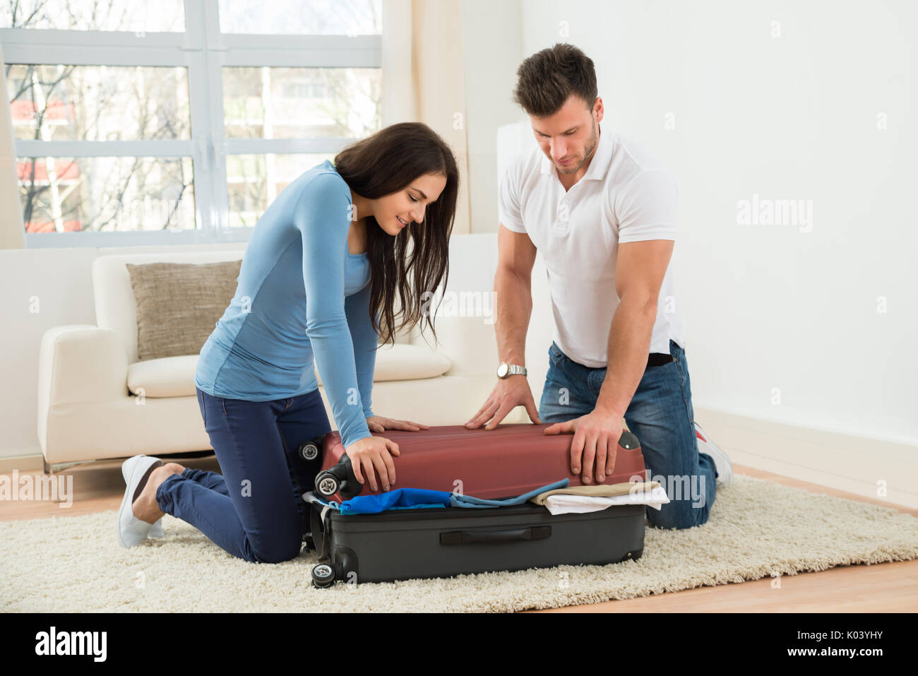 Portrait of Young Smiling Couple essayant de fermer Valise avec beaucoup de vêtements Banque D'Images