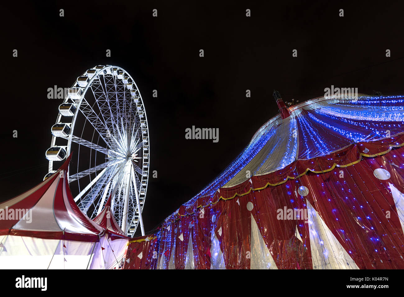 Grande roue illuminée et un chapiteau rouge et blanc tente de cirque tourné de nuit. Banque D'Images