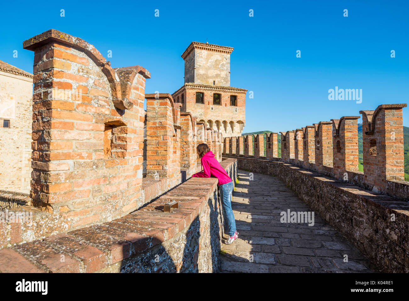 Vigoleno, Piacenza, Italie, Emiglia-Romagna. Femme debout sur les murs du château à la ville ci-dessous. Banque D'Images