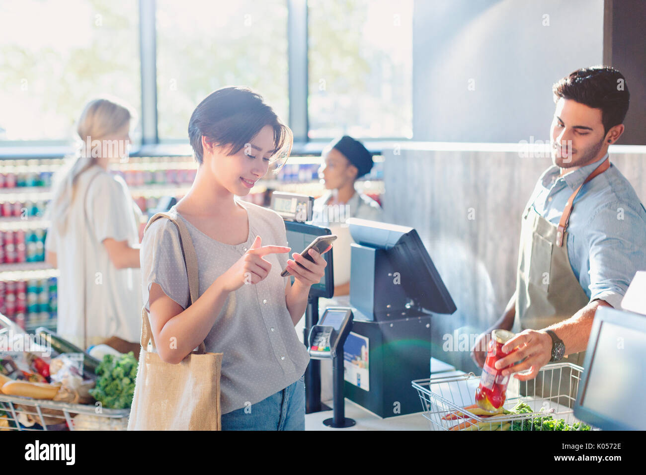 Young woman using cell phone at grocery store commander du marché Banque D'Images