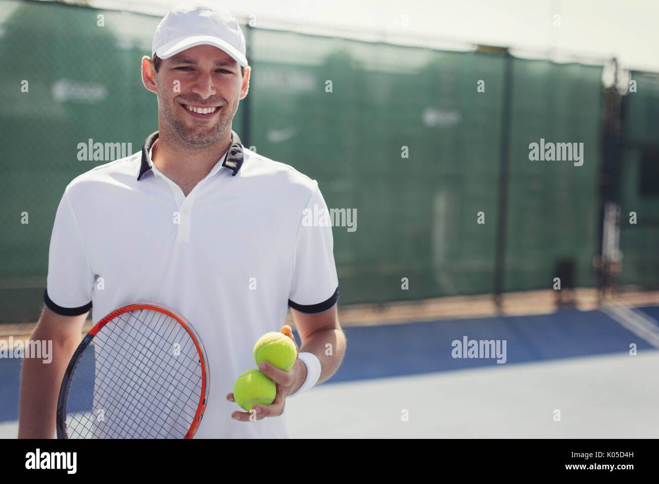 Confiant, Portrait smiling young male tennis player holding raquette de tennis et balles de tennis sur le court de tennis ensoleillé Banque D'Images