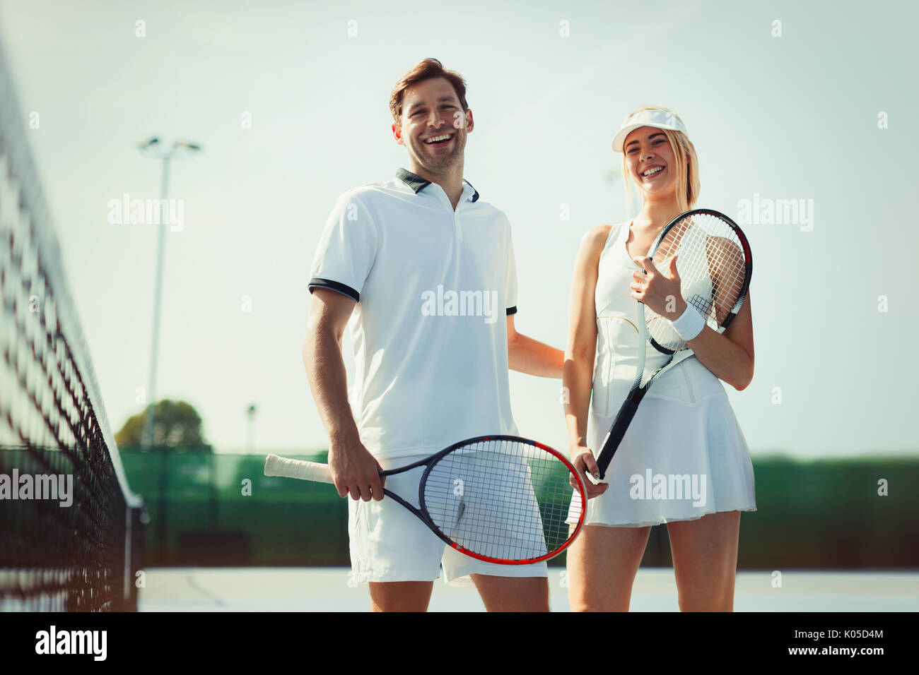 Portrait souriant, confiant la tenue des joueurs de tennis raquettes de tennis sur le court de tennis ensoleillé Banque D'Images