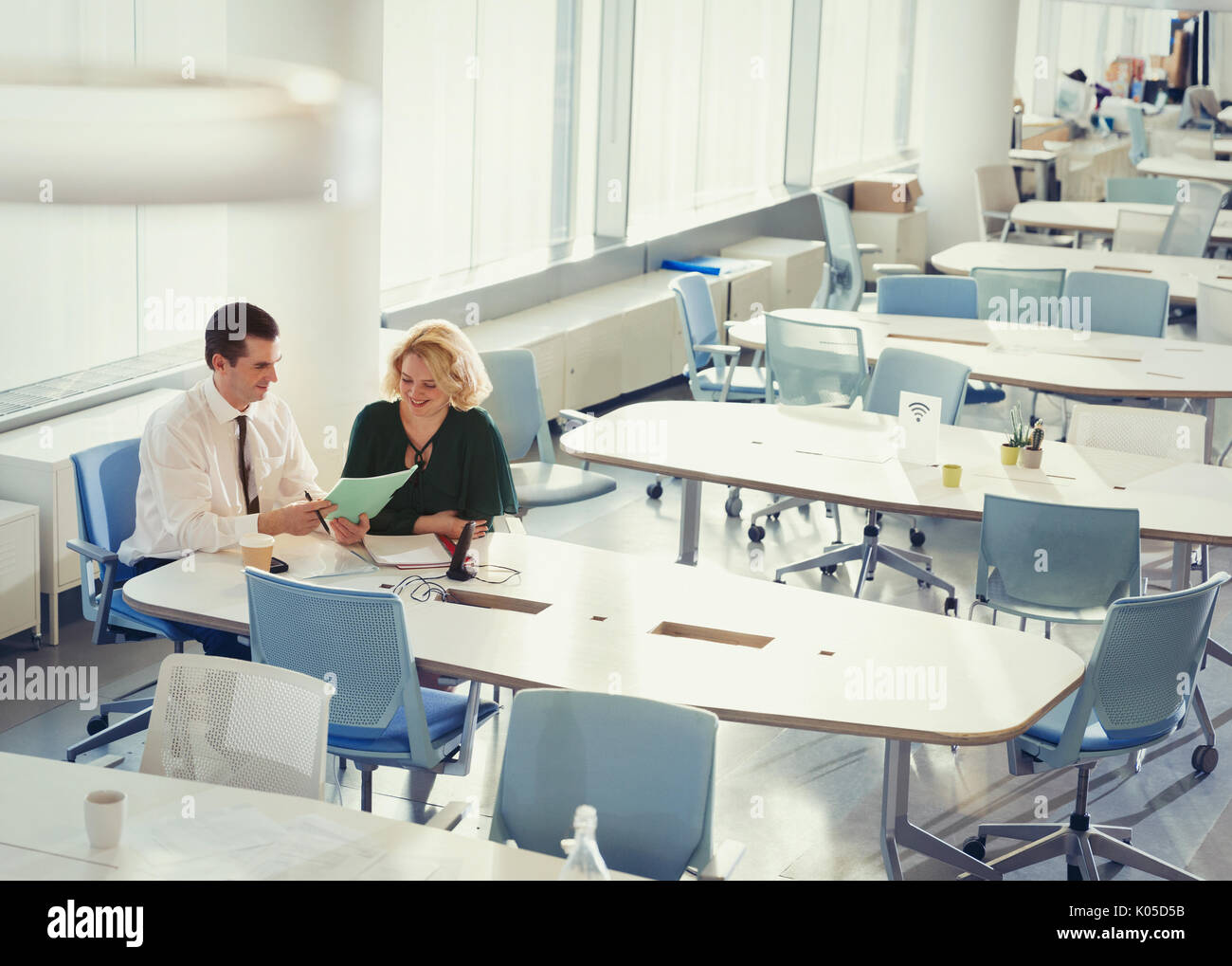Businessman and businesswoman discussing paperwork at table in shared workspace Banque D'Images
