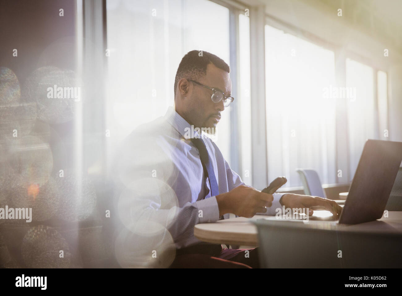 De graves businessman texting with cell phone at laptop in office Banque D'Images