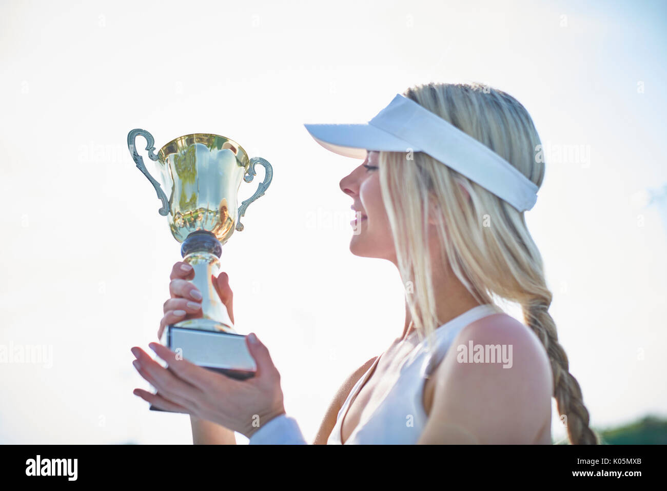 Jeune femme blonde en joueur de tennis visor holding trophée du championnat Banque D'Images