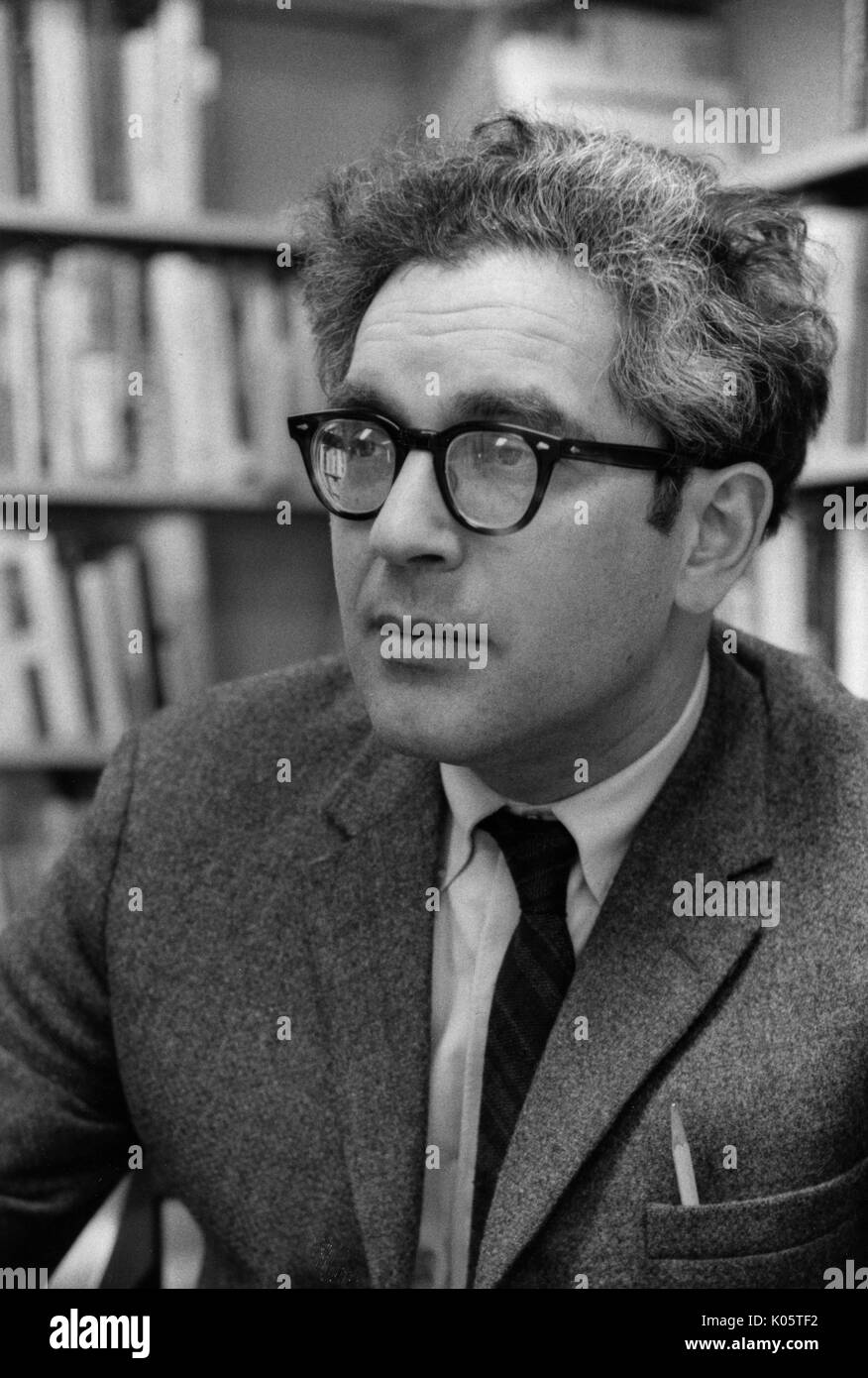 Head-shot portrait du sociologue américain Nathan Glazer, assis dans une bibliothèque, vêtu d'un costume sombre, avec un crayon poussant hors de sa veste en paquet, le port de lunettes sombres, épais, avec une expression du visage, 1969. Banque D'Images