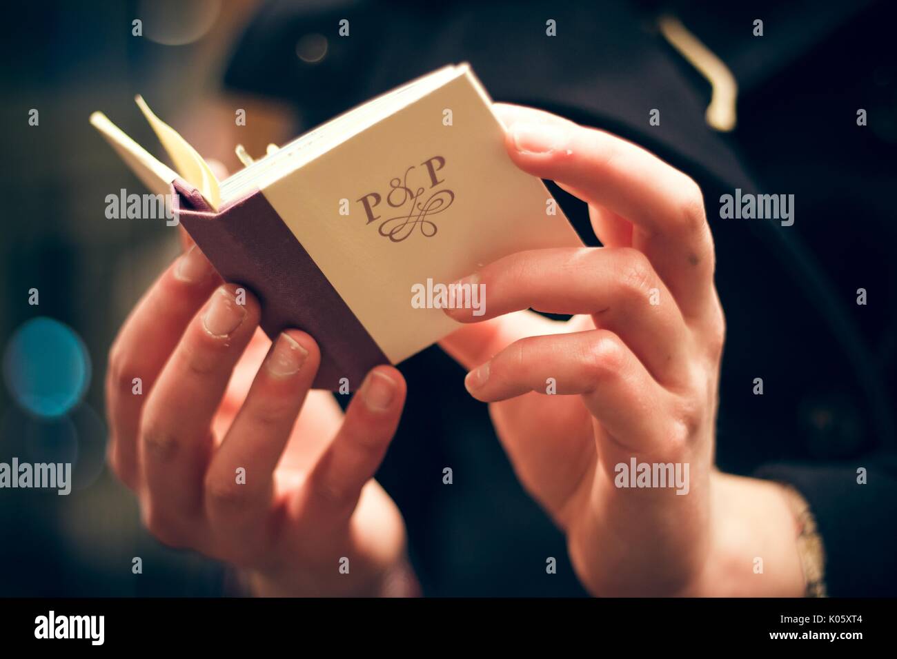 Deux mains tenant un petit livre ouvert avec un couvercle de couleur crème et un dos marron, avec les lettres 'P et P', 2016. Banque D'Images